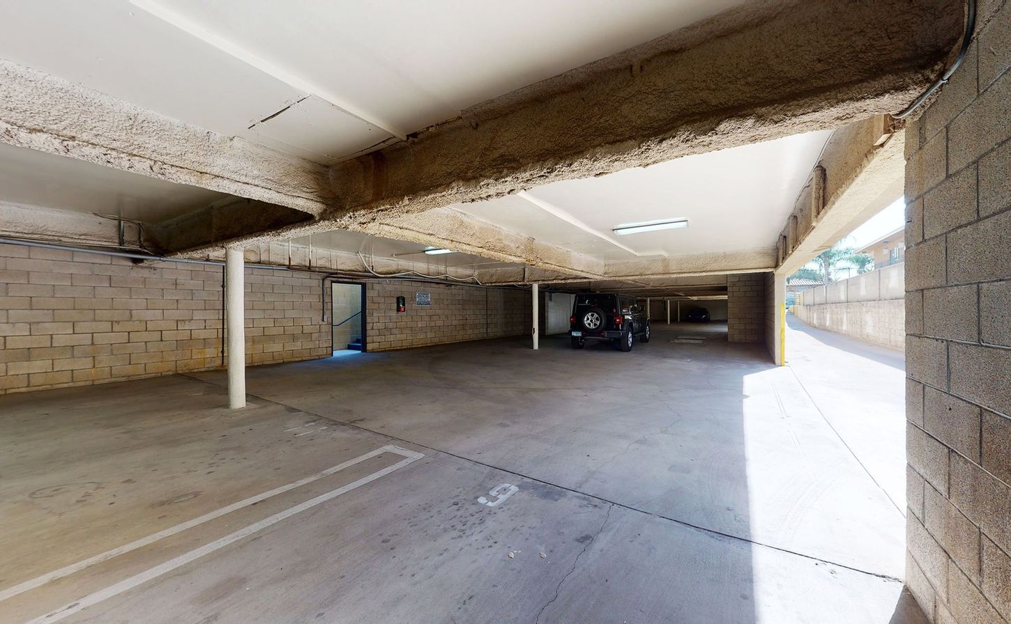 A car is parked in a parking garage under a bridge.