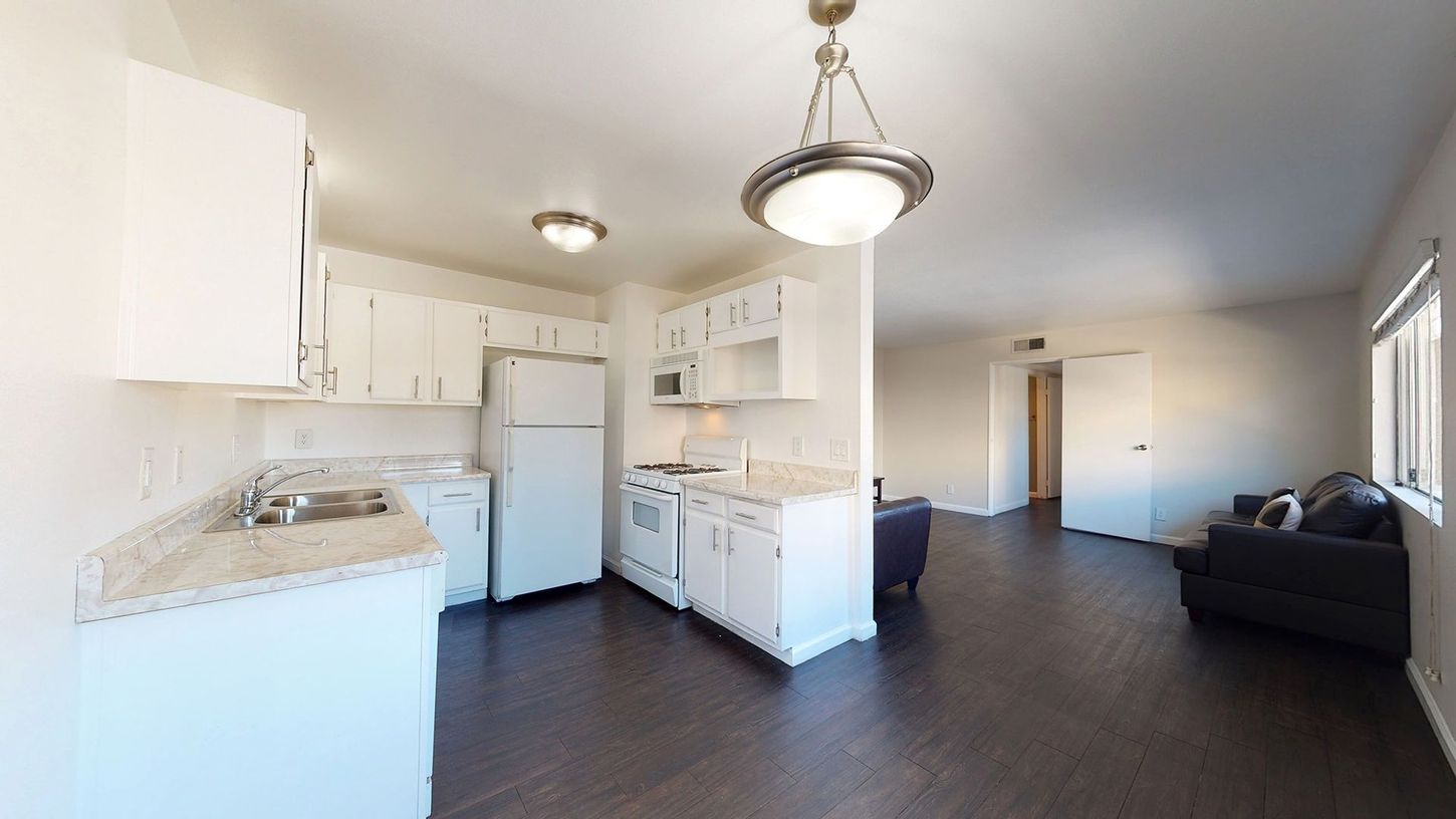 A kitchen with white cabinets , a refrigerator , a microwave , and a couch.