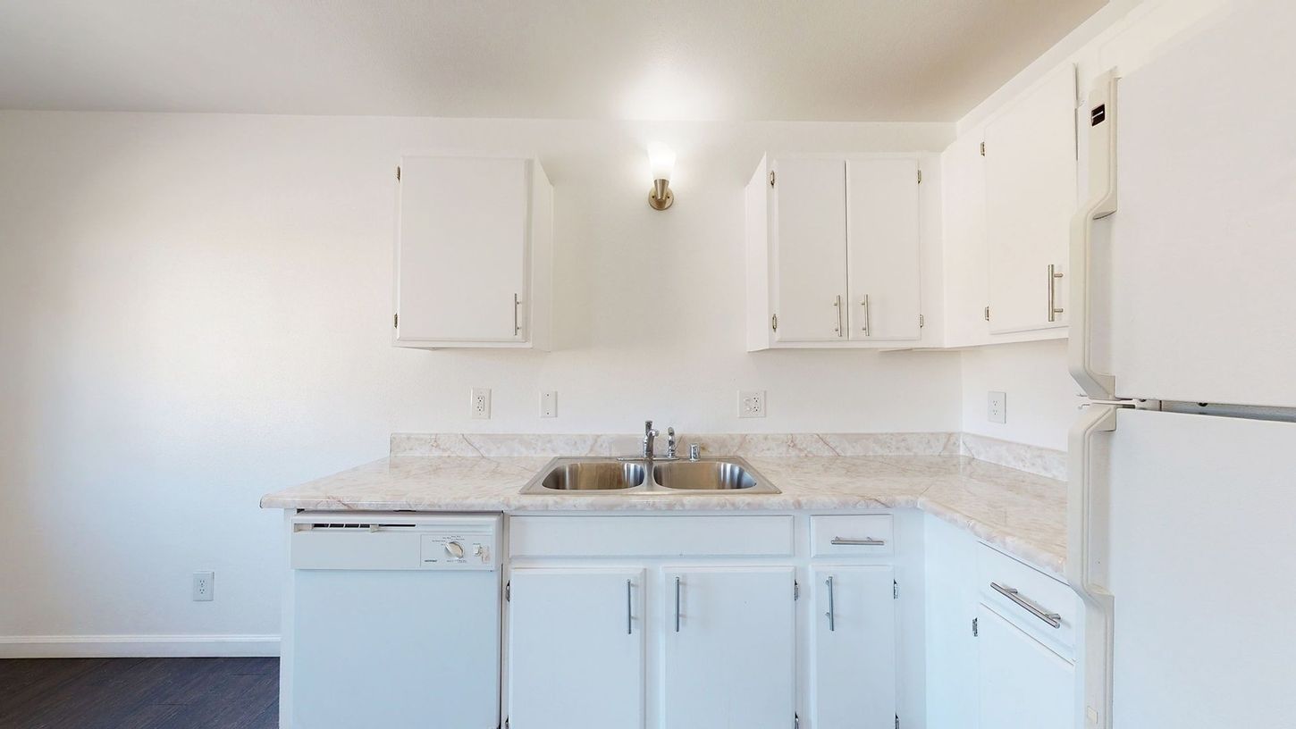 A kitchen with white cabinets , a sink , a refrigerator , and a dishwasher.