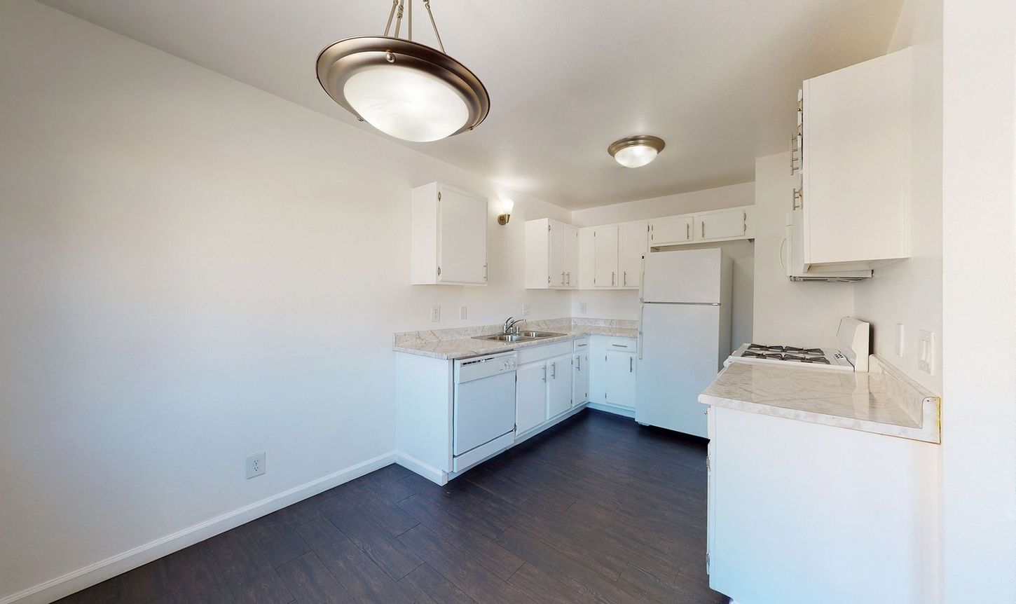 An empty kitchen with white cabinets and a refrigerator.
