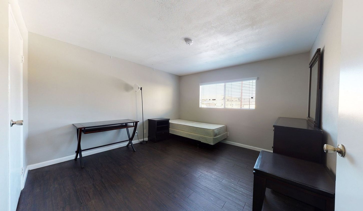 A bedroom with a single bed , dresser , mirror and table.