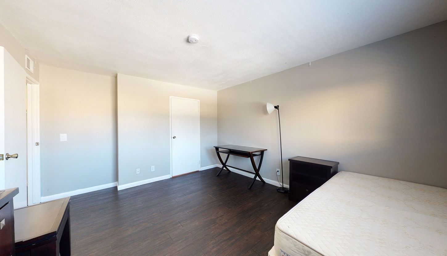 A bedroom with a bed , desk , nightstand and lamp.