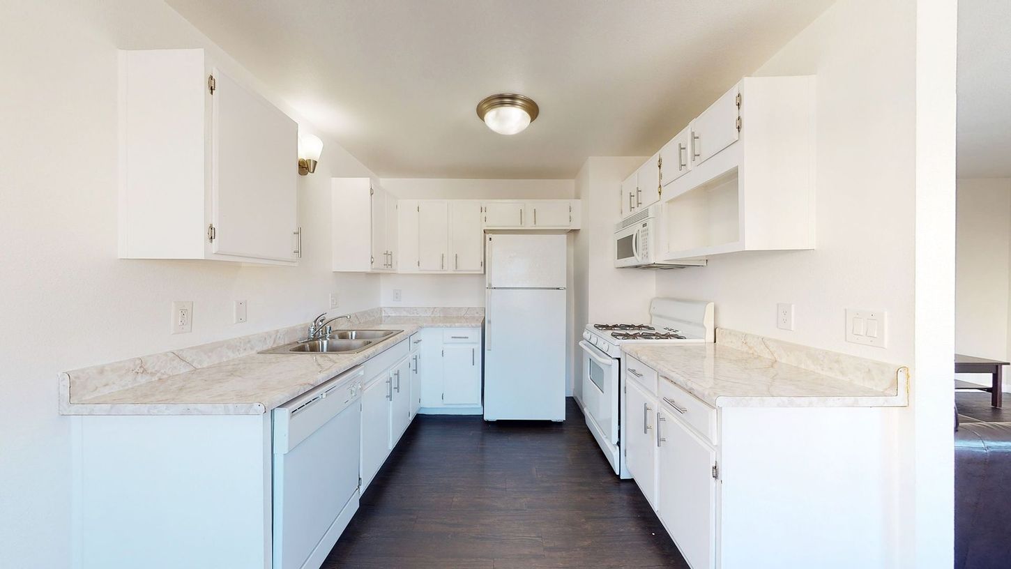 A kitchen with white cabinets , a refrigerator , a stove , and a sink.