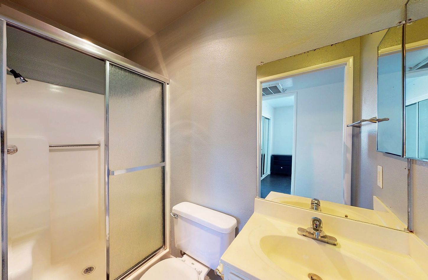 A bathroom with a toilet , sink , shower and mirror.