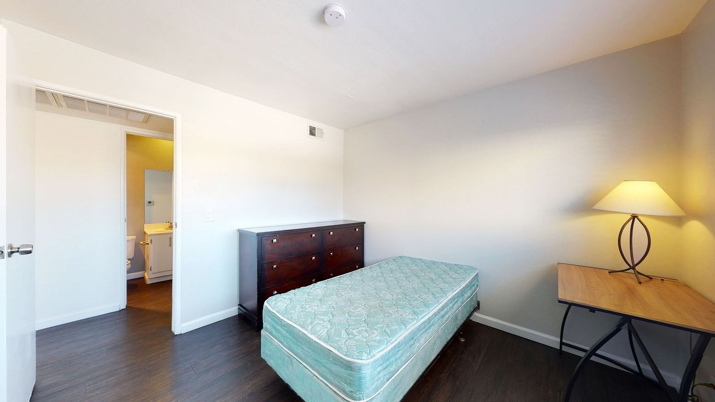A bedroom with a bed , desk , lamp and dresser.
