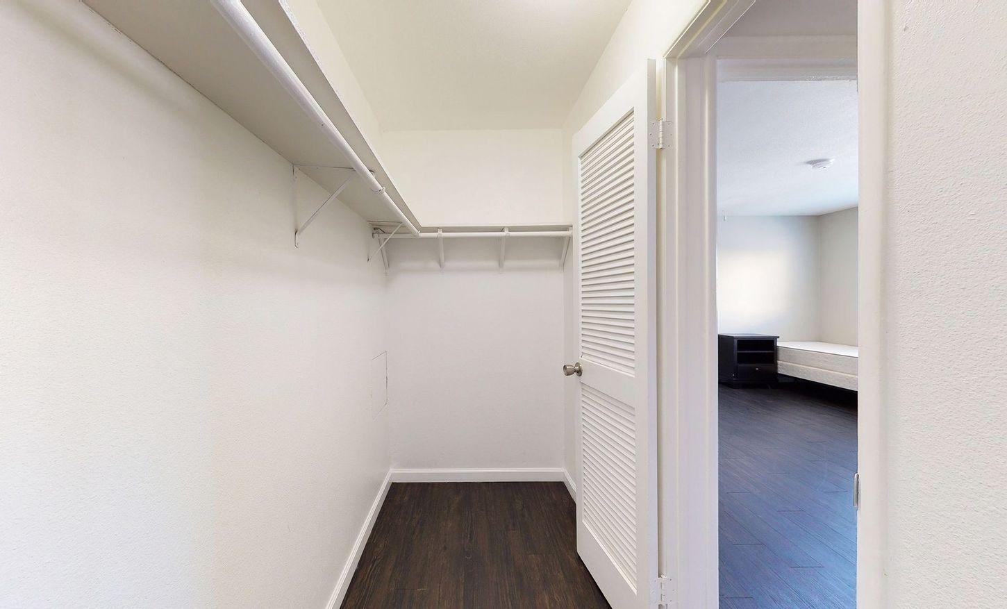 A walk in closet with a door open to a bedroom.