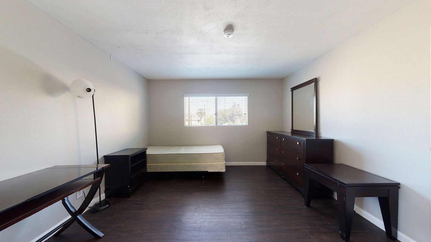 A bedroom with a bed , dresser , mirror and table.