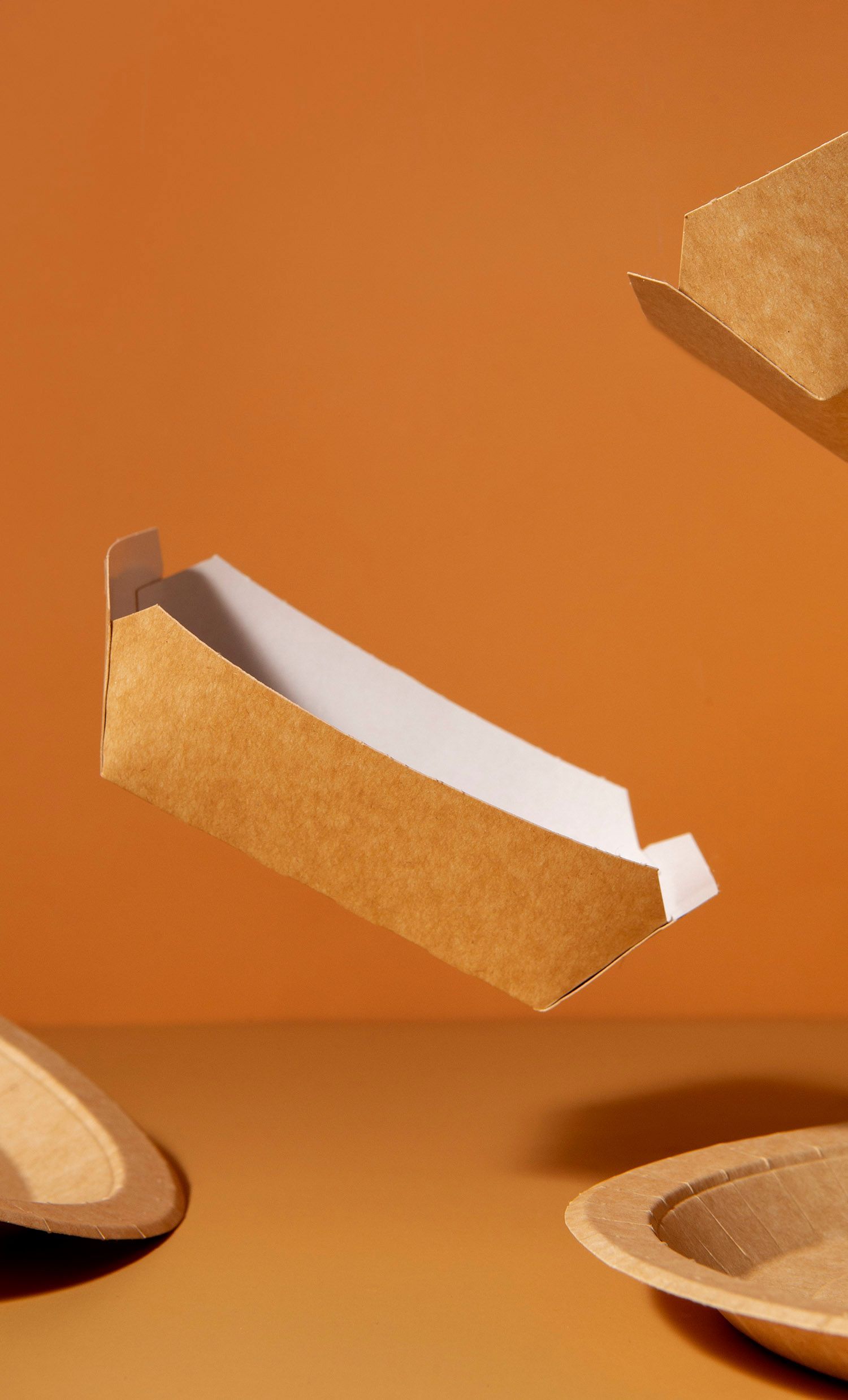 Brown and white cardboard food trays floating against an orange background.