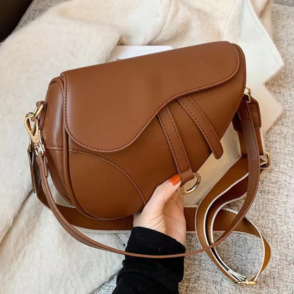 a person is holding a brown saddle bag with a long strap .