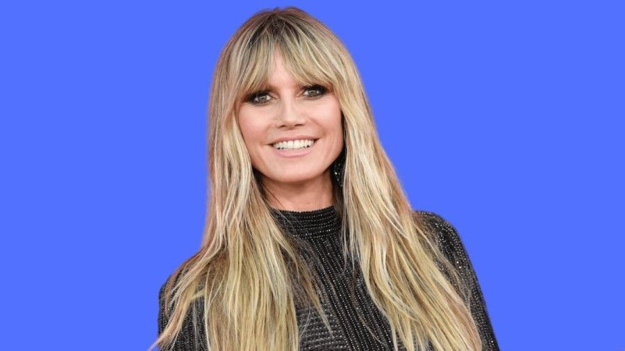 a woman with long blonde hair is smiling in front of a blue background .