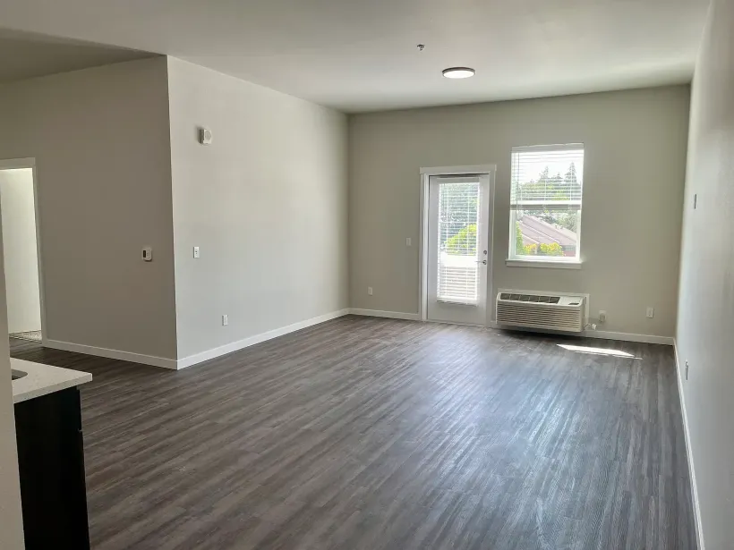 An empty living room with hardwood floors and a sliding glass door.