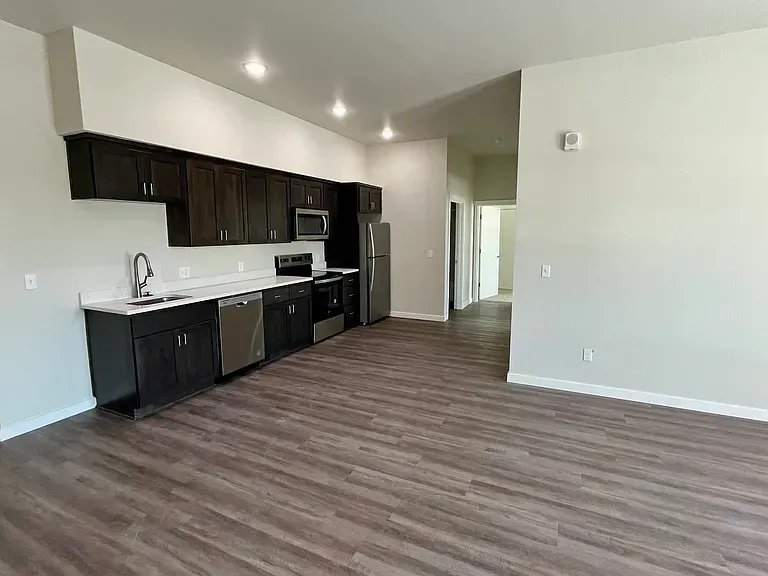 A kitchen with stainless steel appliances and wooden floors in an empty apartment.