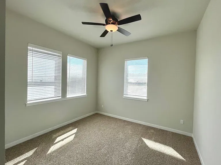 An empty bedroom with a ceiling fan and two windows.