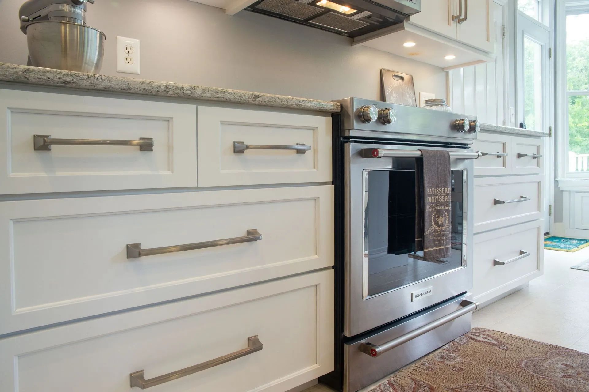 Bright white kitchen with gray countertops, stainless steel oven, and white cabinets with brushed metal handles