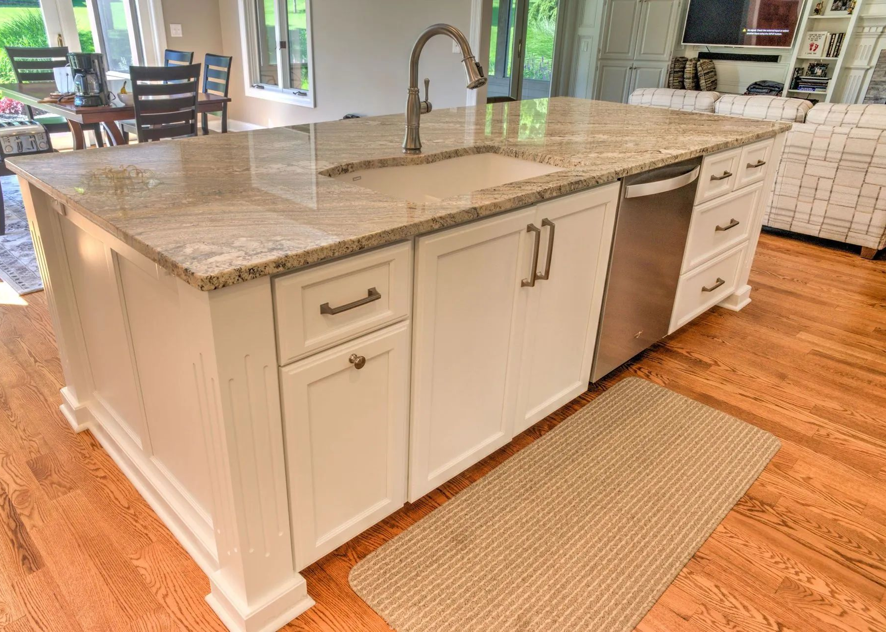 White kitchen island with granite countertop, built-in sink, and hardwood floor in a bright open kitchen