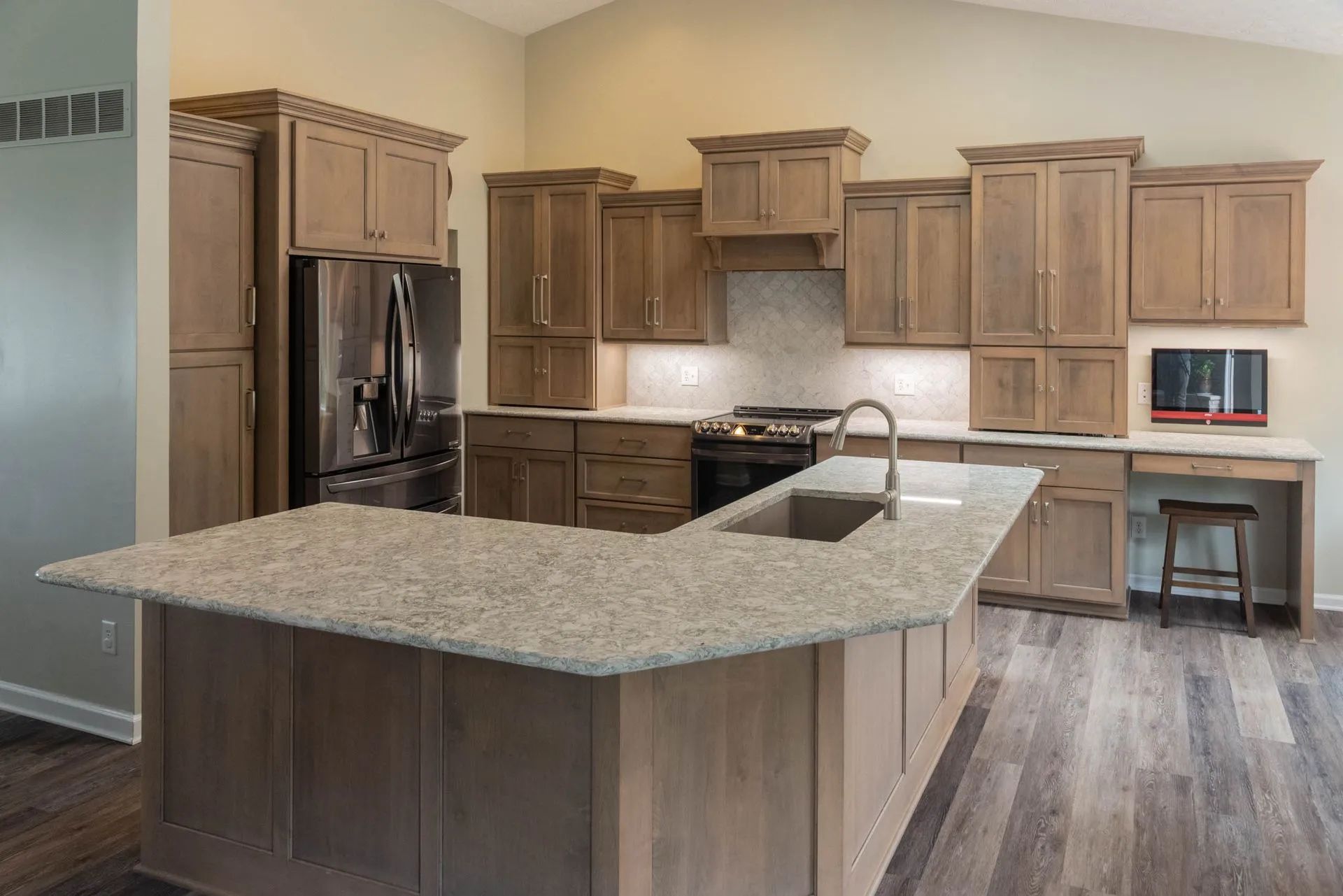 Spacious kitchen with wood cabinets, granite island, stainless fridge, and a small desk nook.