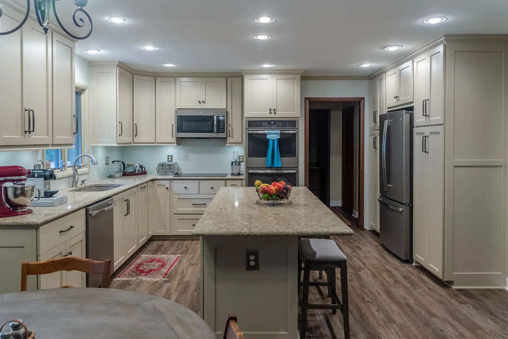 Bright modern kitchen with white cabinets, granite island, stainless appliances, and wood-look floors