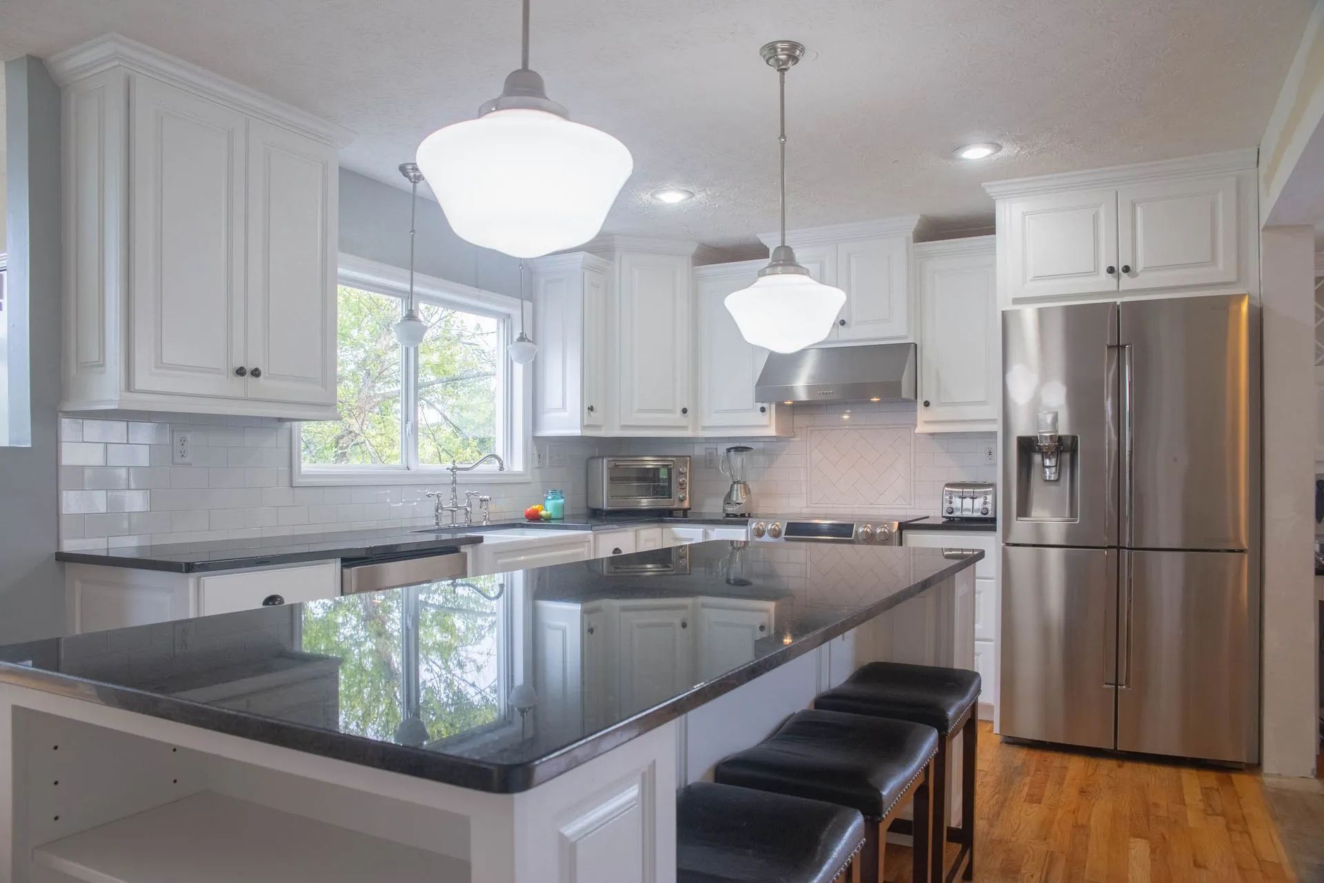 Modern kitchen featuring white cabinets, black countertops, a central island with bar seating, and stainless steel fridge.