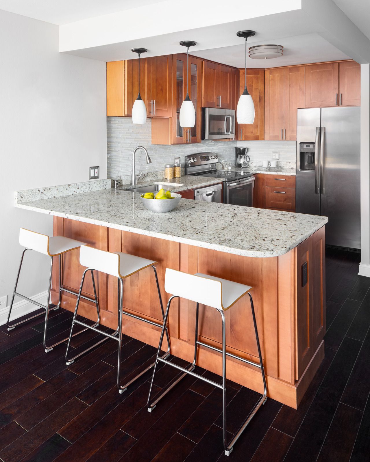 Modern kitchen with wood cabinets, white countertop, island with stools, stainless steel appliances.