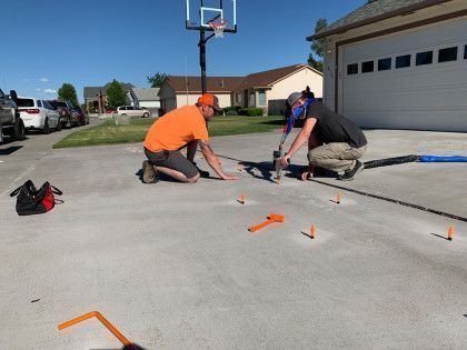 Two men kneeling on concrete driveway, working on leveling with tools and markers.
