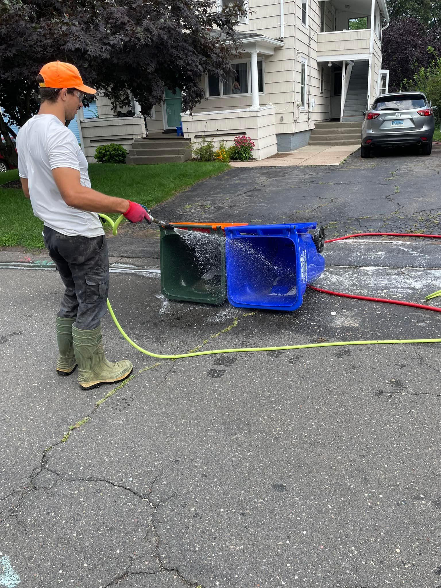 A man is cleaning a trash can with a hose.