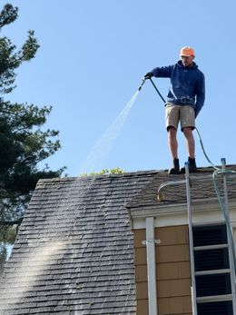A man on a ladder spraying water on a roof