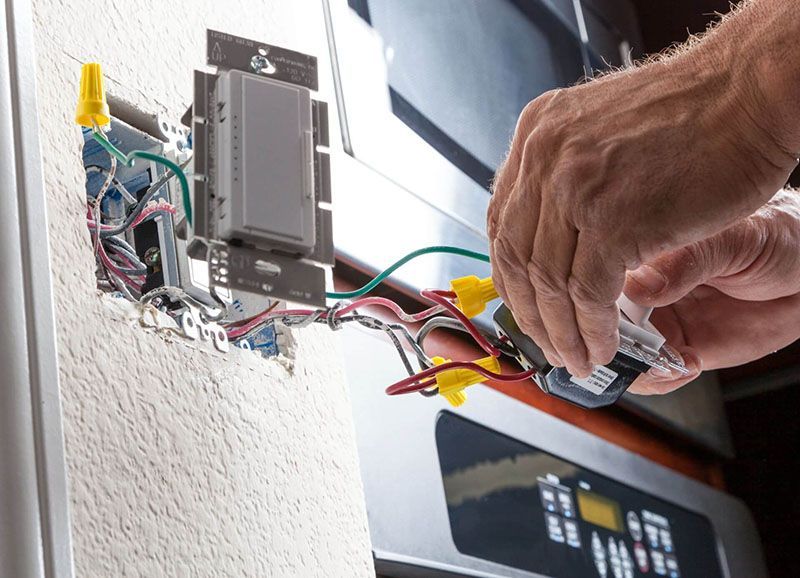 Una persona sta cablando un interruttore elettrico in una parete. I fili sono collegati con connettori, le mani sono al lavoro.