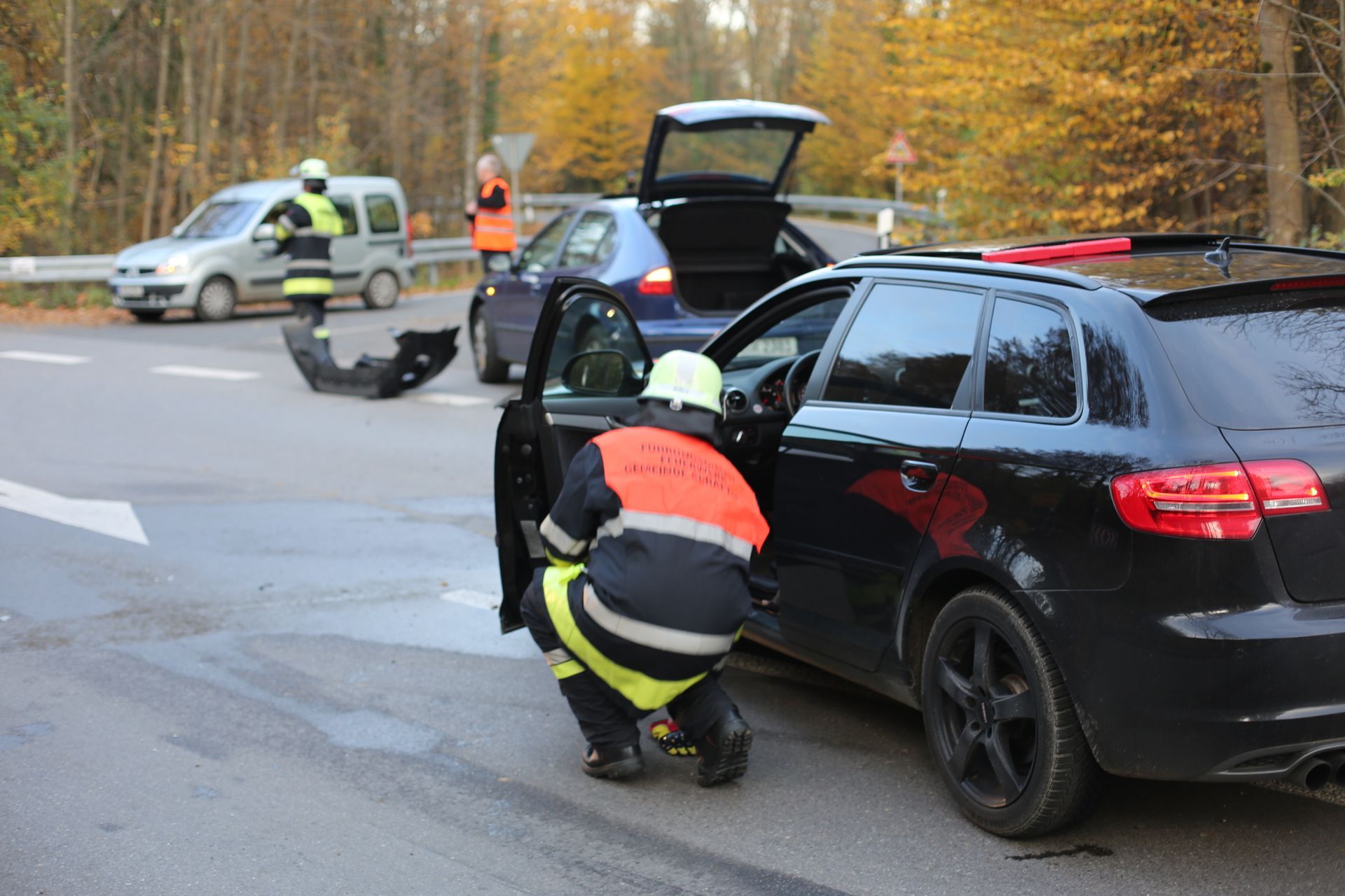 Firefighter at car accident scene; two cars damaged, other emergency personnel nearby.