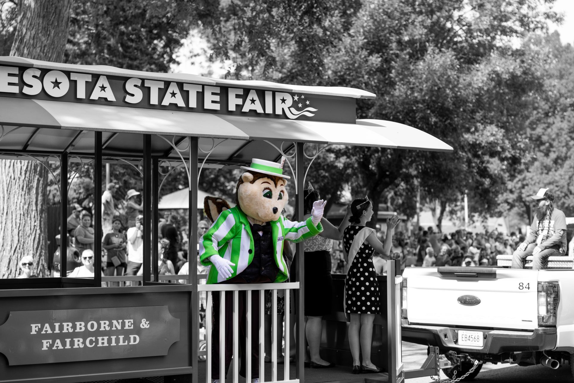 A gopher mascot is standing on a trolley at the Minnesota State Fair.