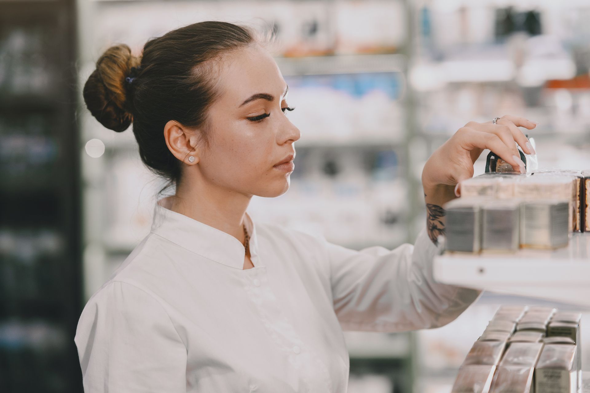 Atendente de farmácia organizando prateleira de skincare e dermocosméticos comprados no atacado.
