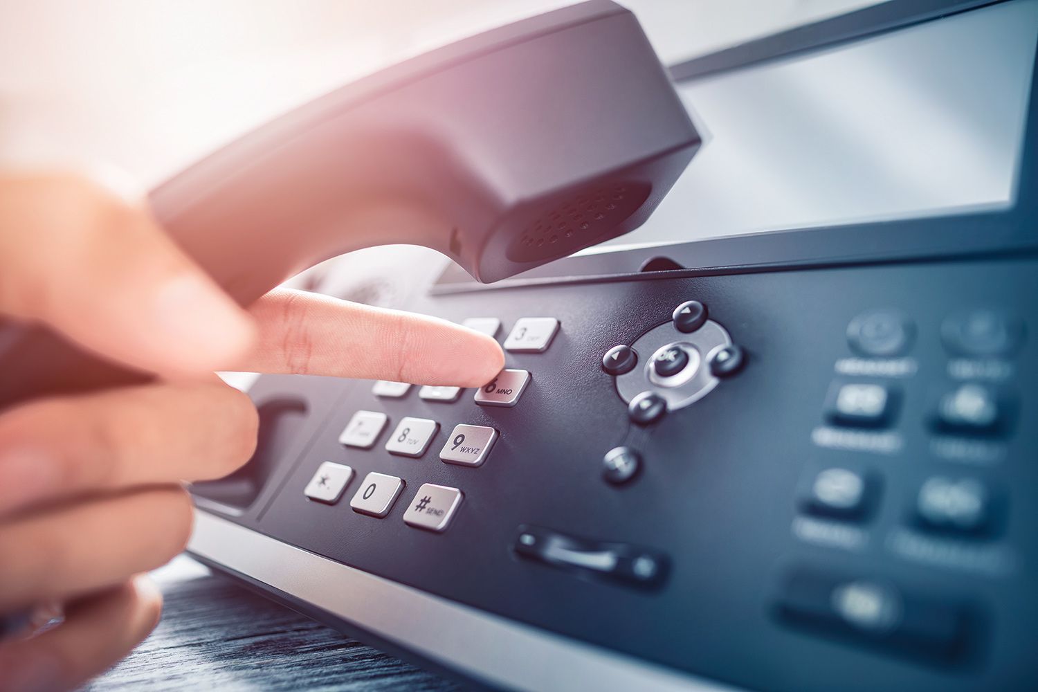 Hand dialing a number on a black office phone Hand dialing a number on a black office phone