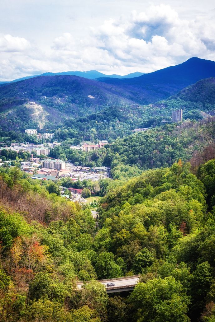 Lush green mountain valley with scattered buildings under a cloudy blue sky