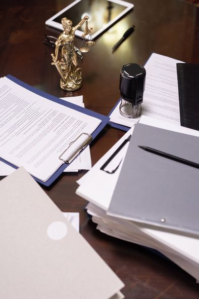 Desk with stacked papers, open notebook, pen, and office supplies on a dark table