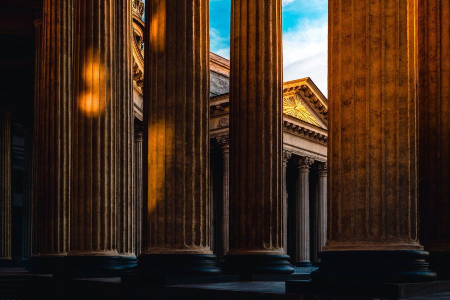 Sunlit classical columns framing a neoclassical building under a blue sky