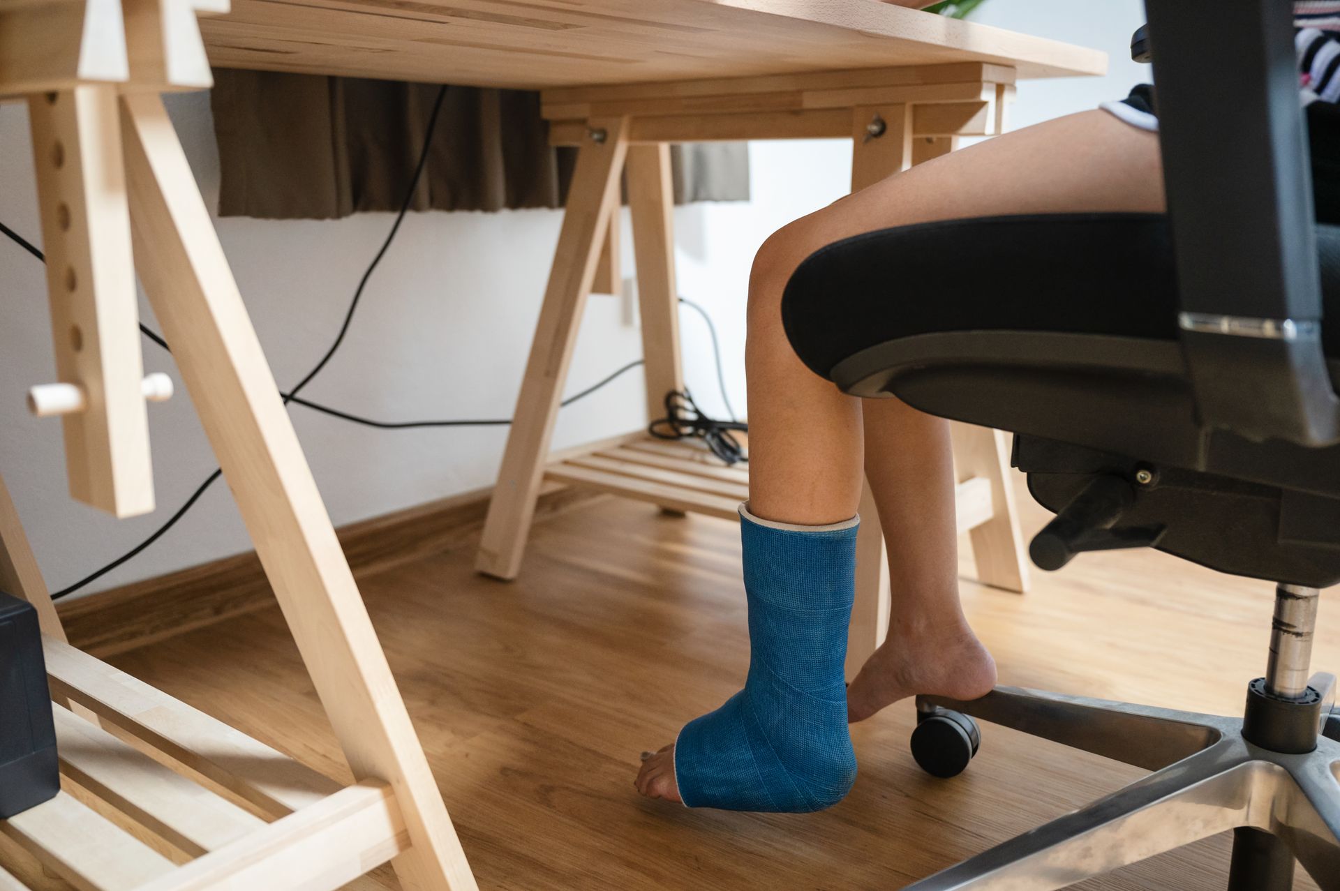 Person in a black office chair under a desk, wearing blue socks in a home workspace.