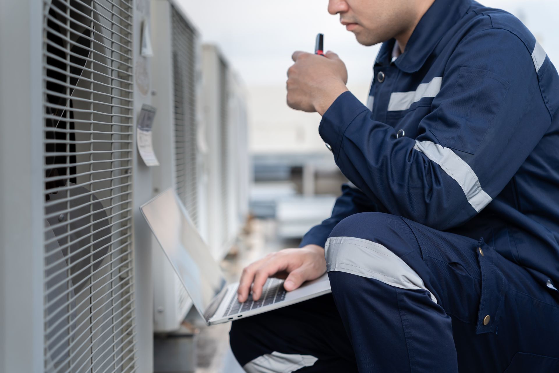 A technician using a laptop to note AC unit maintenance on a roof.