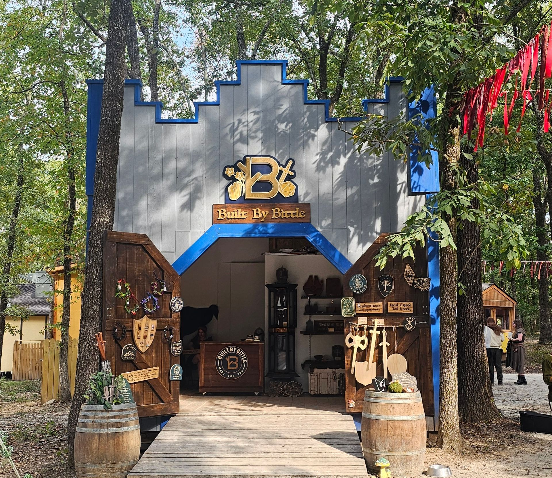Shopfront with wooden door, selling medieval-themed goods. Sign says "Bottle of Beer". Trees surround.