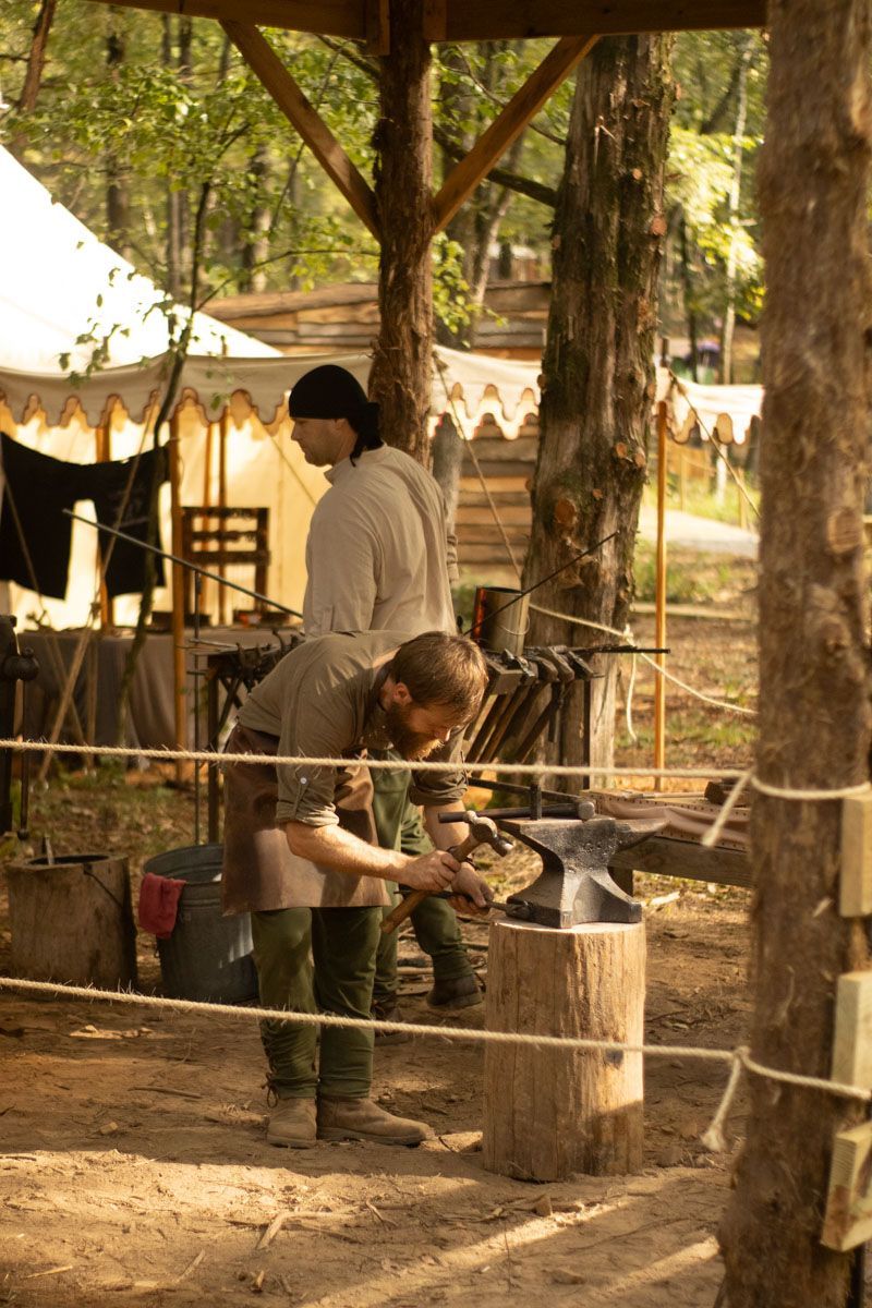 Two people chopping wood beside a small shelter in a wooded outdoor camp area