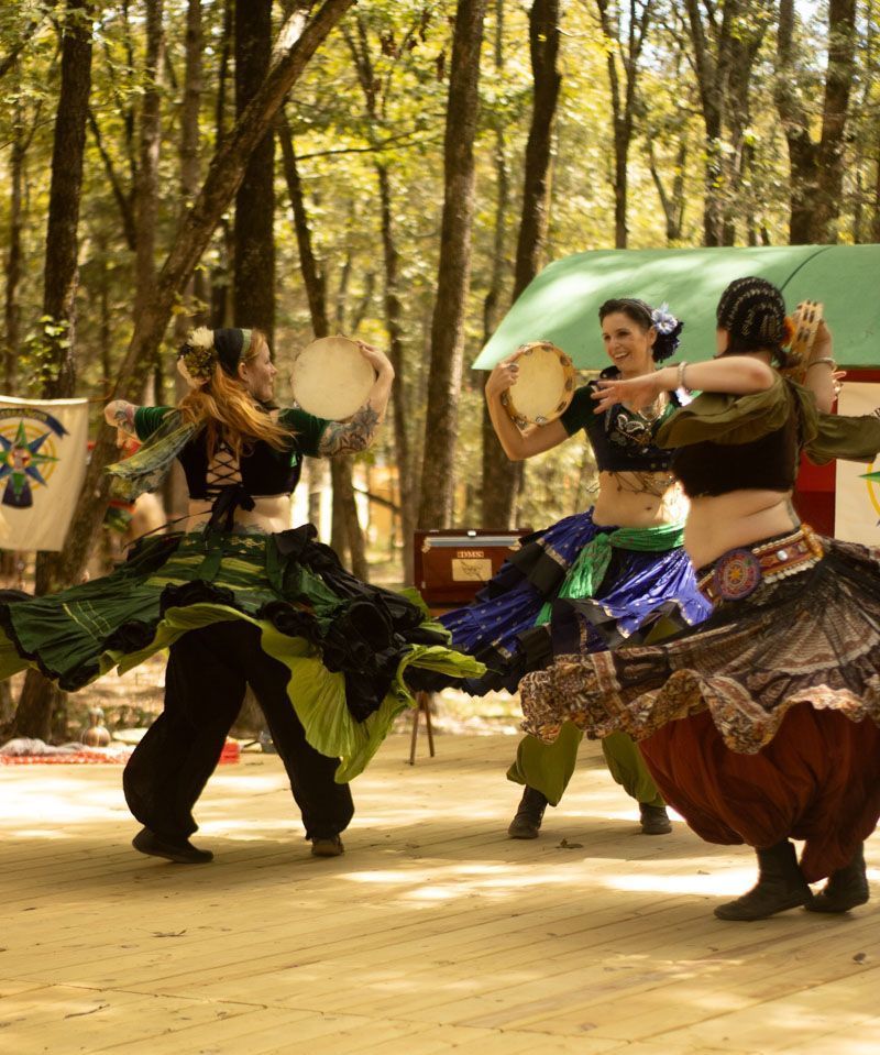 A group of women are dancing and playing tambourine in the woods