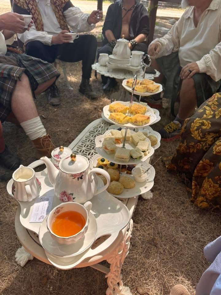 Tea and snacks on a tiered serving stand at an outdoor gathering, with people seated around it
