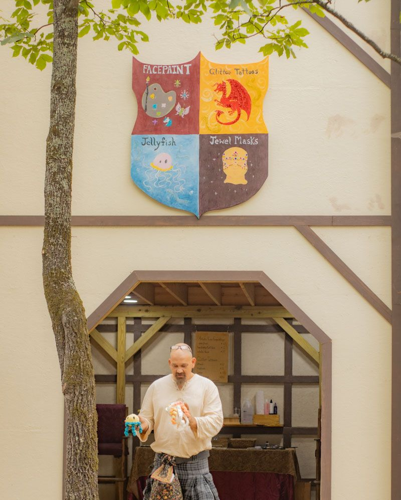Man holding puppets beneath a medieval-style building with a crest of fantasy creatures.