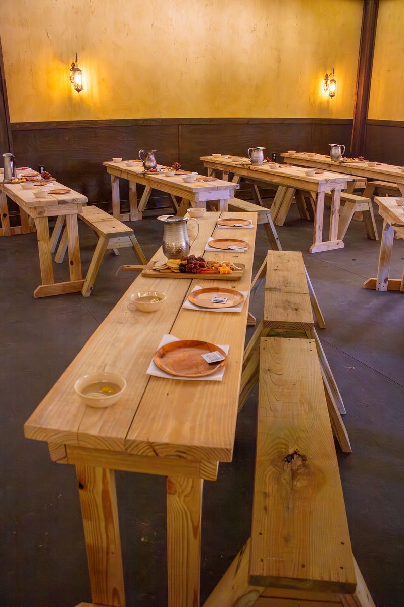 Rustic dining room with long wooden tables, benches, and plates set for guests
