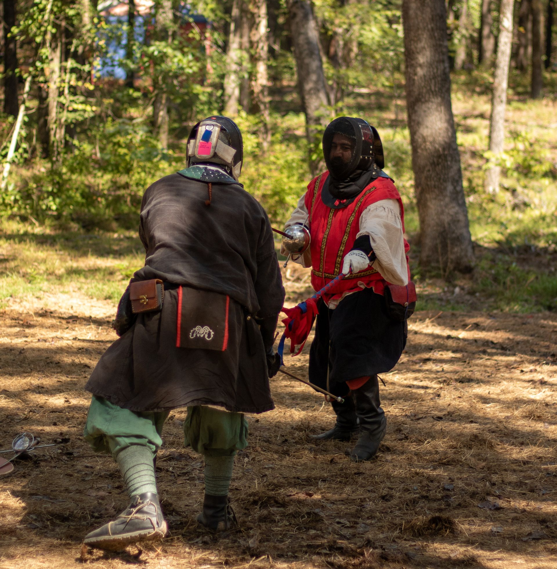 Two armored fighters in a wooded clearing, one in red and white, facing each other with weapons raised.