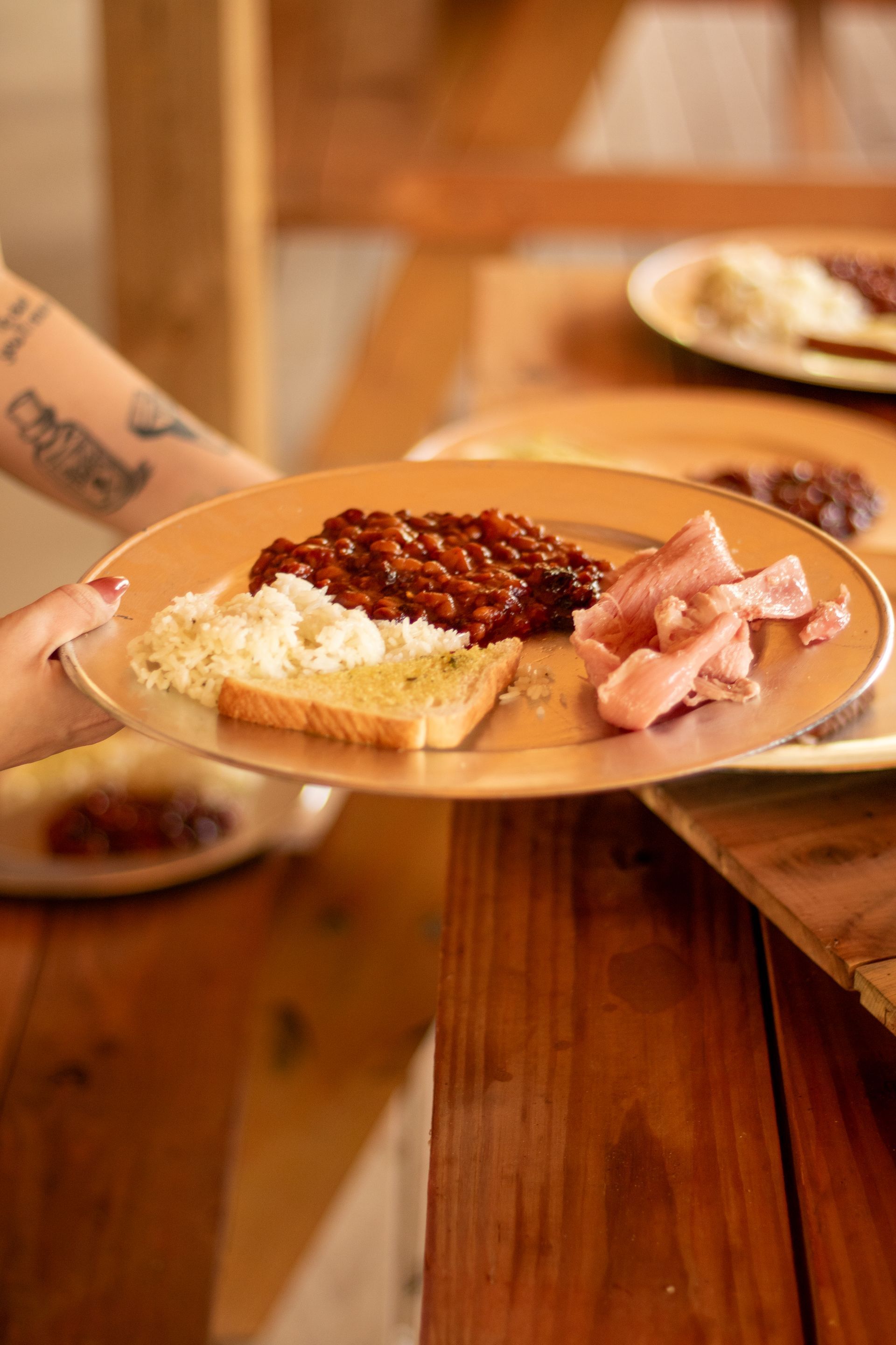 Plate with breakfast foods held over a wooden table: beans, eggs, toast, and bacon