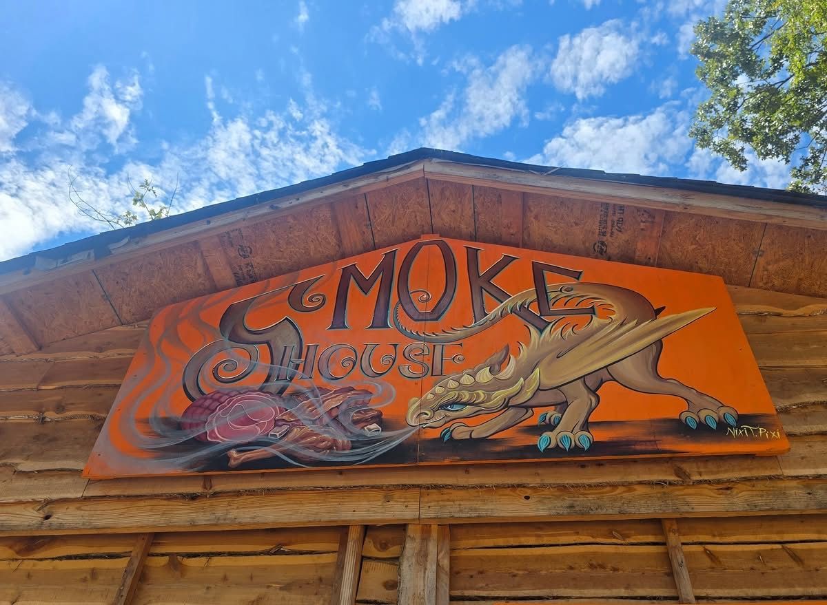Orange “SMOKE” sign with fish illustration on a rustic wooden building under a blue sky