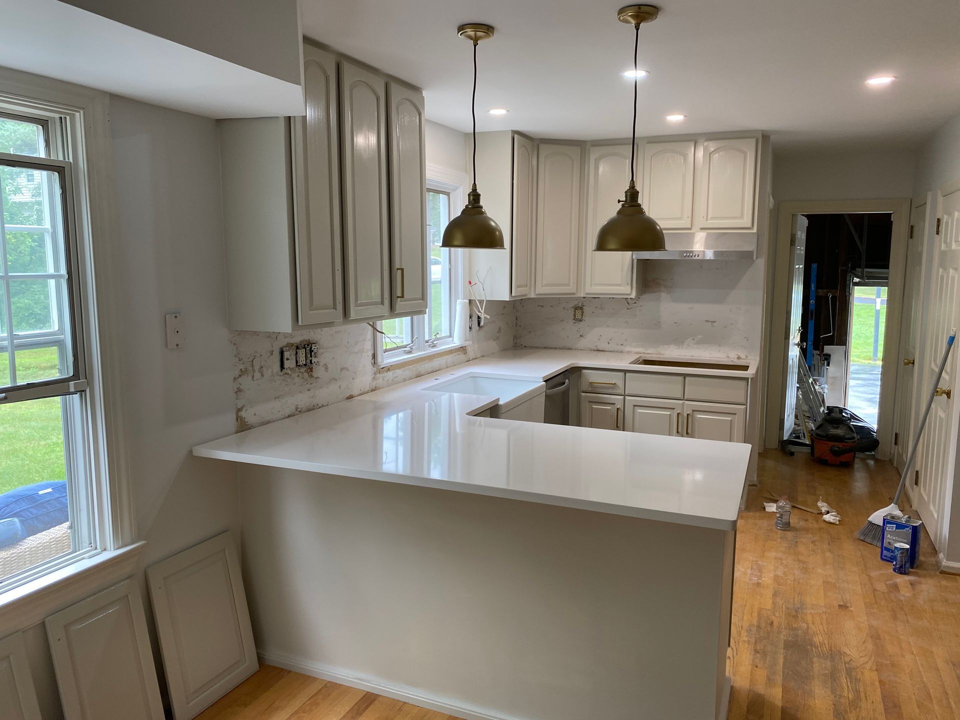 Kitchen with white cabinets, countertops, and pendant lights; doorway on right; window on left.