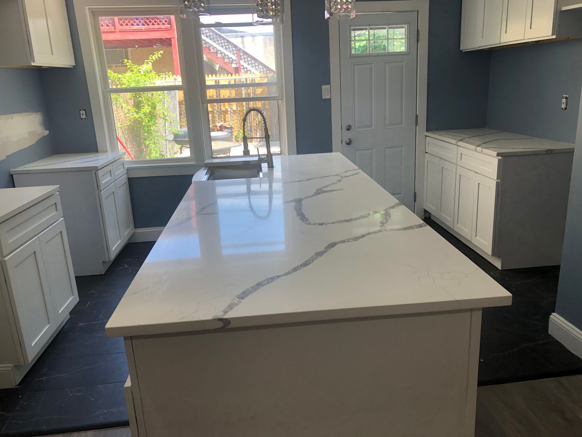 White kitchen with a large island, marble countertop, and blue walls.