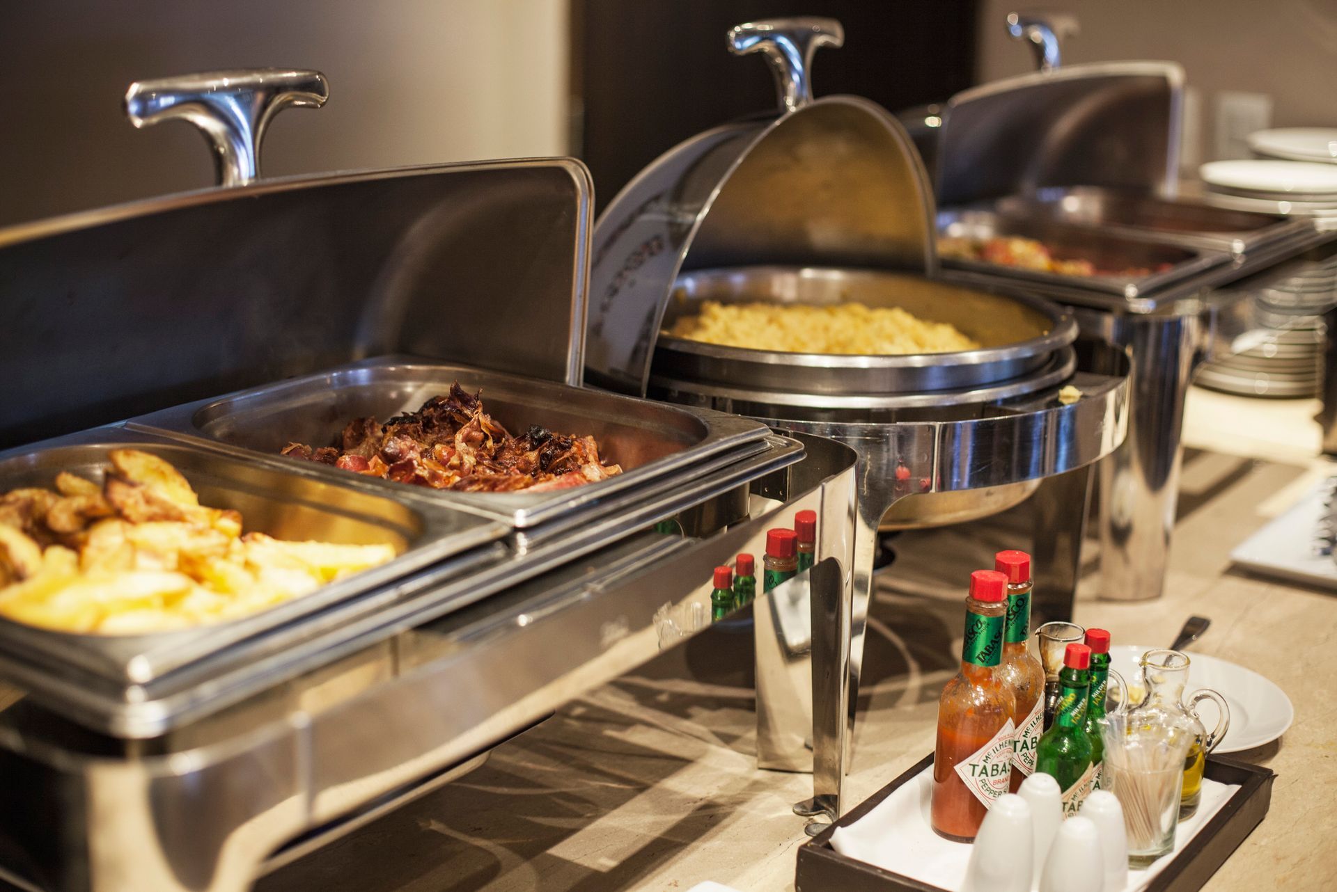 Buffet con vari piatti caldi serviti in scaldavivande d'argento. Include patate, carne e contorni.