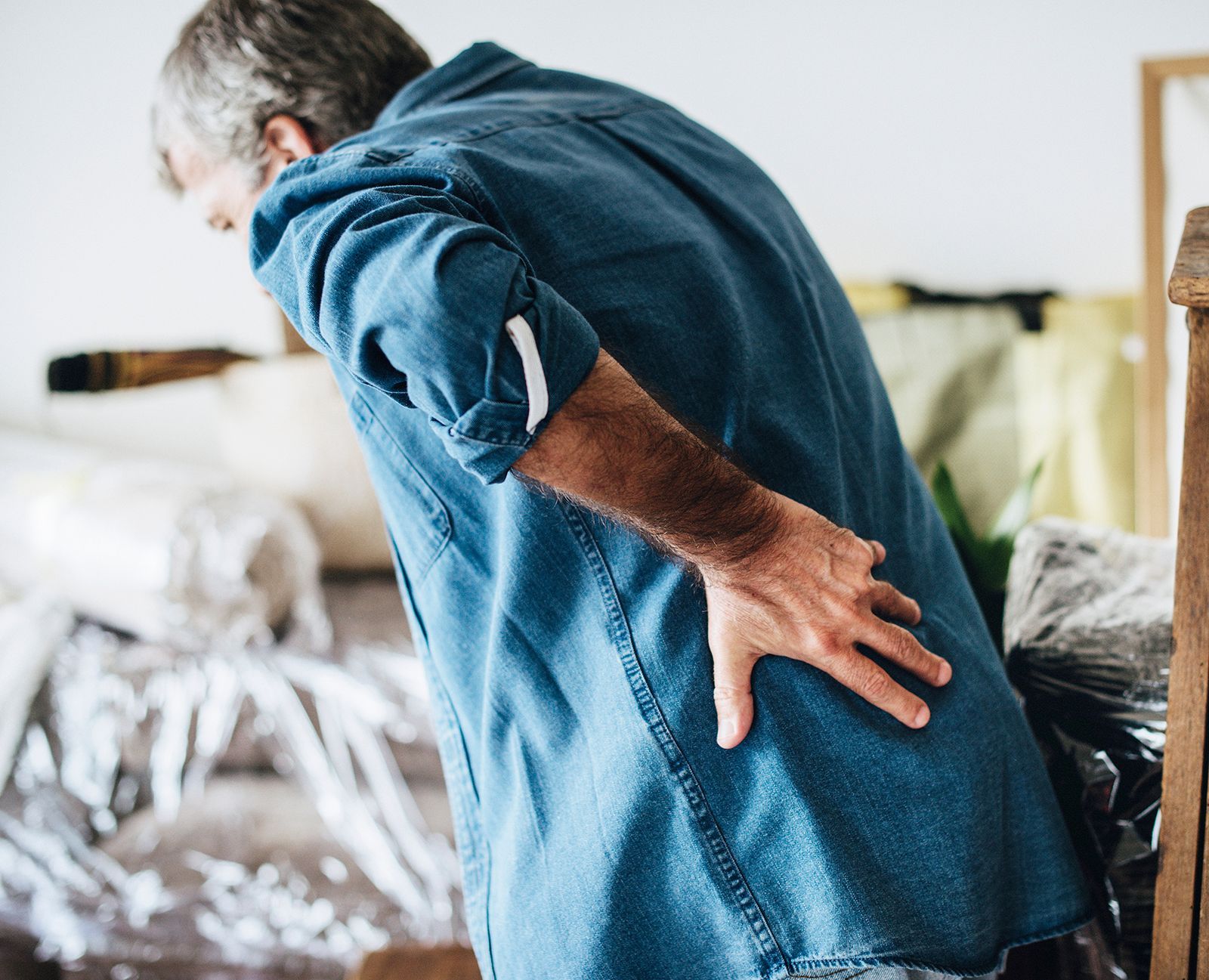 Hombre agarrándose la espalda baja con dolor, posiblemente debido a que levantó un objeto pesado durante una mudanza.