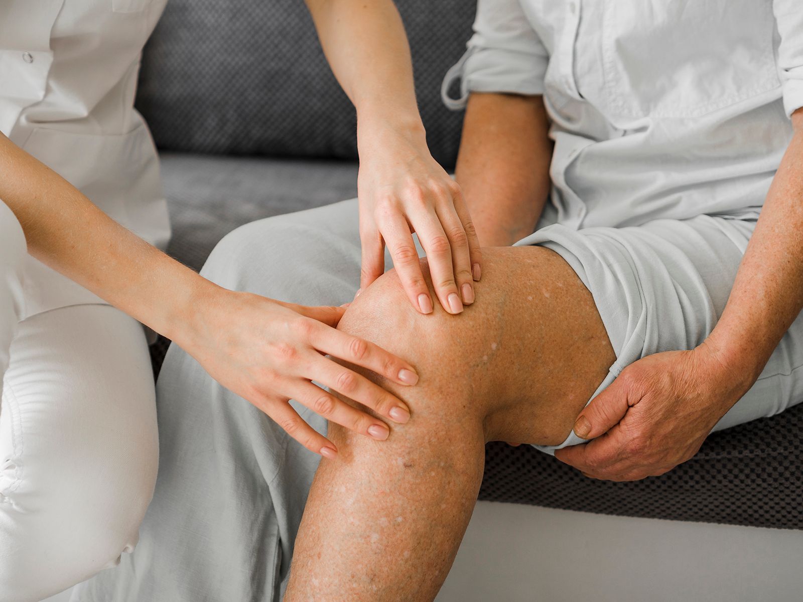 Un profesional médico examina la rodilla de una persona en un diván para evaluar si hay dolor o lesión.